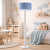 Nowoczesna lampa podłogowa z niebieskim abażurem w przytulnym pokoju dziecięcym. Stylowe wnętrze pełne detali, pastelowe dodatki i funkcjonalny design idealny do aranżacji przestrzeni dla dziecka.