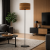 Nowoczesna lampa podłogowa z drewnianym abażurem i czarną, minimalistyczną podstawą idealnie wpisuje się w aranżację salonu w stylu modernistycznym. Połączenie naturalnego drewna i czerni tworzy elegancki, ponadczasowy design wnętrza.