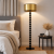 Nowoczesna lampa podłogowa z elegancką, złotą abażurą i designerską podstawą z czarnych, połyskujących kul. Idealna do sypialni i salonu, zapewnia nastrojowe oświetlenie oraz stylowy akcent w aranżacji wnętrza.