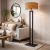 Nowoczesna lampa podłogowa o minimalistycznym designie z czarną, metalową podstawą i eleganckim, drewnianym abażurem. Idealna do salonu, sypialni lub biura. Zapewnia ciepłe, przytulne światło i stylowe wykończenie wnętrza.