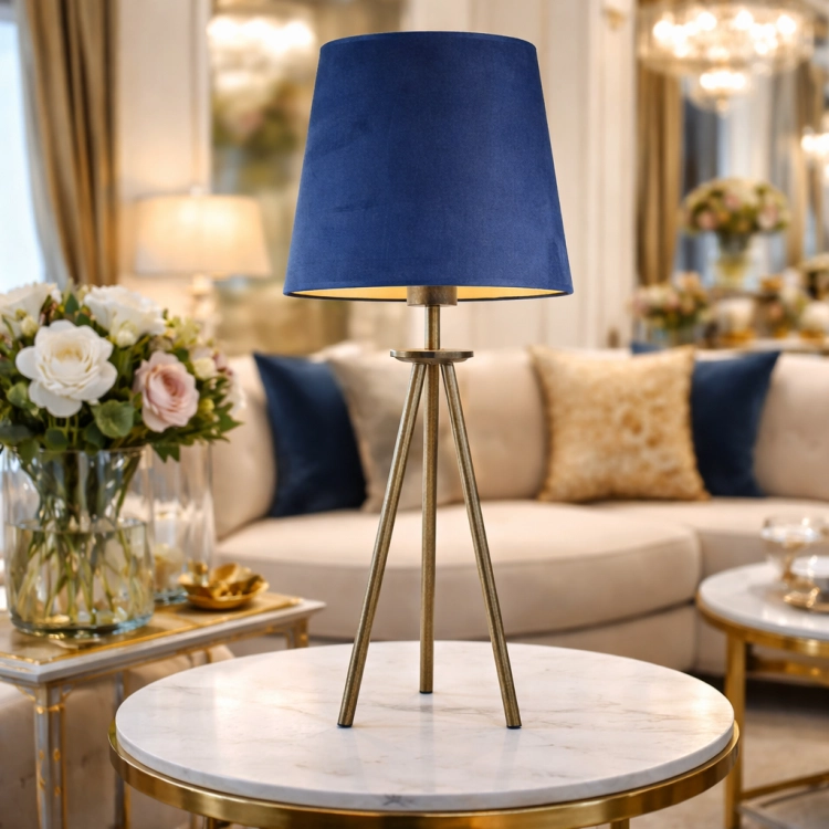 Elegancka lampka stołowa na trójnogu z mosiężnym wykończeniem i granatowym abażurem idealnie wpisuje się w styl glamour. Ustawiona na marmurowym stoliku stanowi stylowy akcent wnętrza, dodając mu luksusu, ciepła i wyjątkowego charakteru.