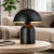 Nowoczesna czarna lampka stołowa o designerskiej formie typu „mushroom”. Minimalistyczny kształt, matowe wykończenie i ciepłe światło tworzą elegancki klimat w salonie, sypialni lub biurze. Idealna do wnętrz nowoczesnych i loftowych.